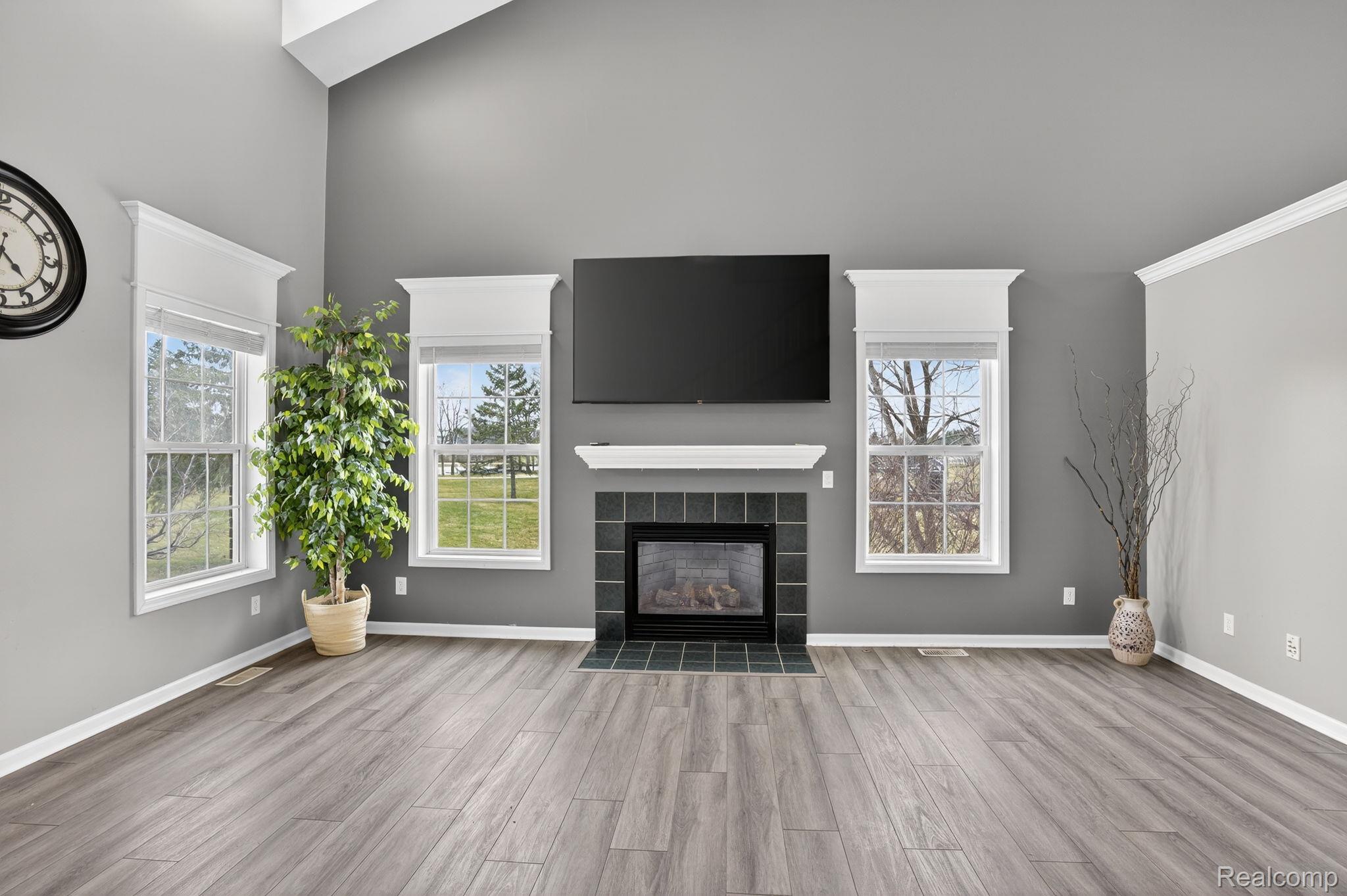 9055 Hegel Road Grand Blanc, MI 48439 - Photo 19 of 62 Living area featuring a fireplace with a black tile surround and white mantle, two double-hung windows with white trim, vaulted ceilings, and wood-finish flooring