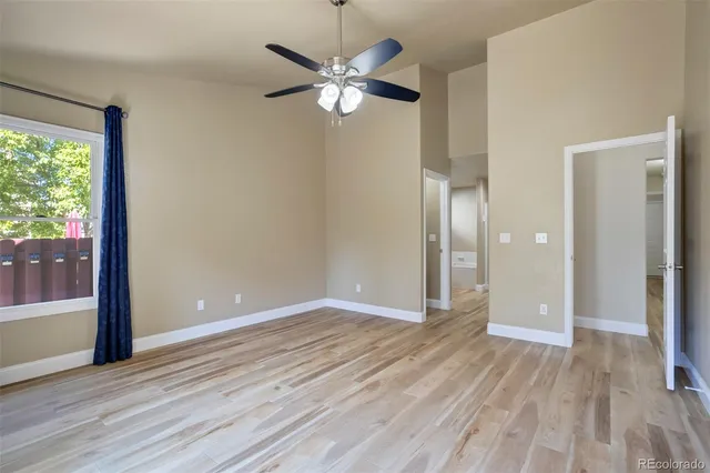 a view of an empty room with wooden floor and a ceiling fan