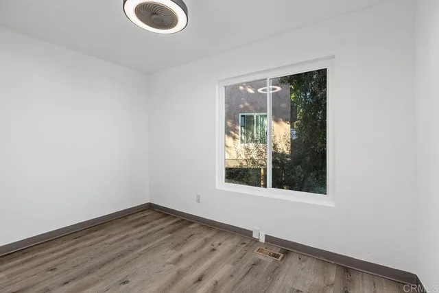 an empty room with wooden floor ceiling fan and windows