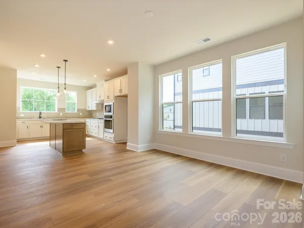 a view of an empty room with wooden floor and a kitchen