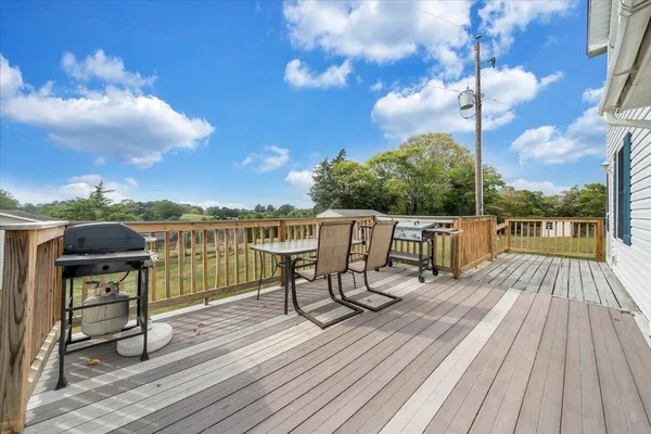 a view of a roof deck with table and chairs a barbeque with wooden floor and fence
