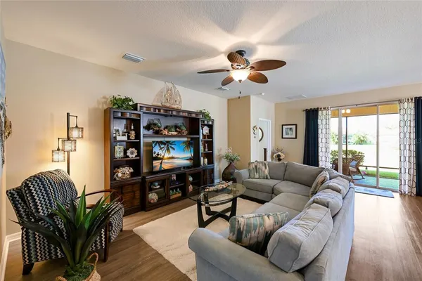 a living room with furniture a ceiling fan a flat screen tv and a large window