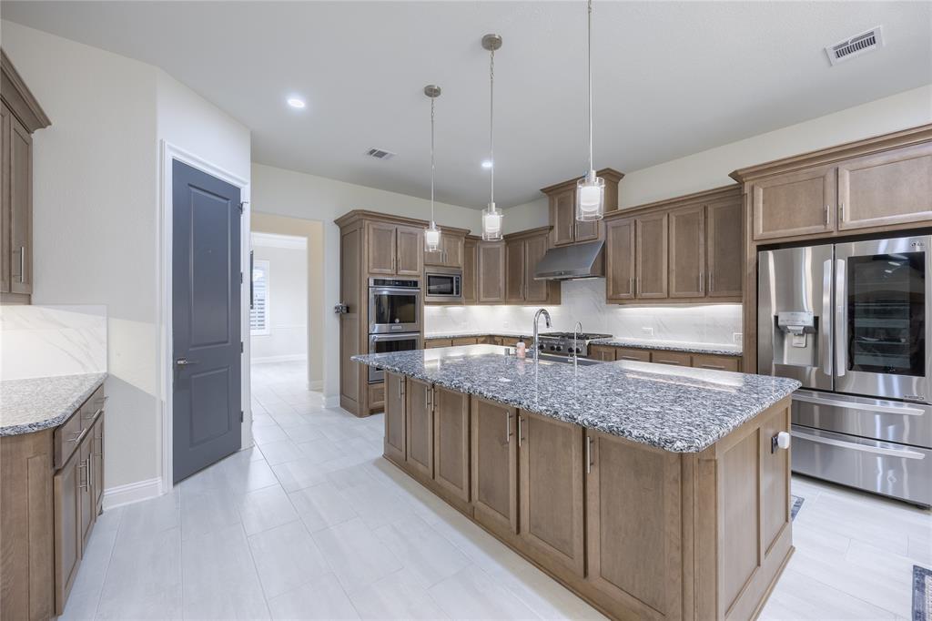 918 Sydney Lane Allen, TX 75013 - Photo 11 of 40 The kitchen features an expansive island with a granite countertop, pendant lighting, stainless steel appliances, and wood cabinetry throughout
