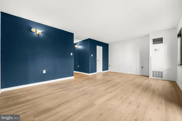 a view of an empty room with wooden floor and kitchen view