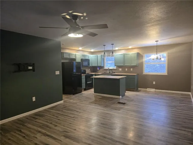 an empty room with wooden floor kitchen view and a window