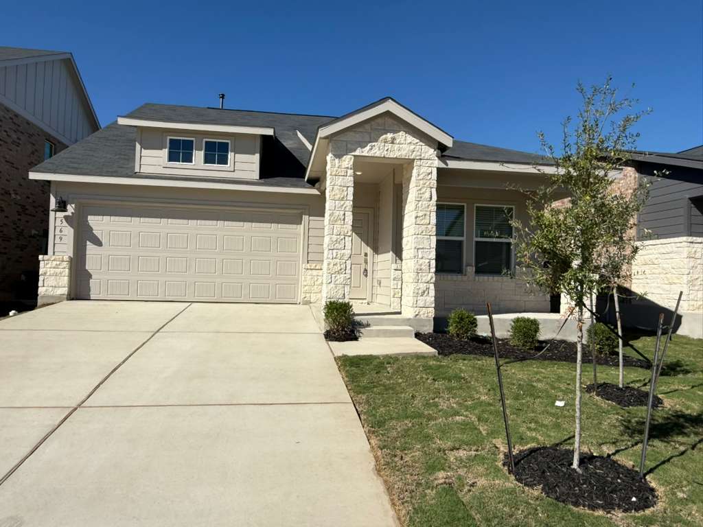 View of front facade featuring stone siding, driveway, and a front lawn