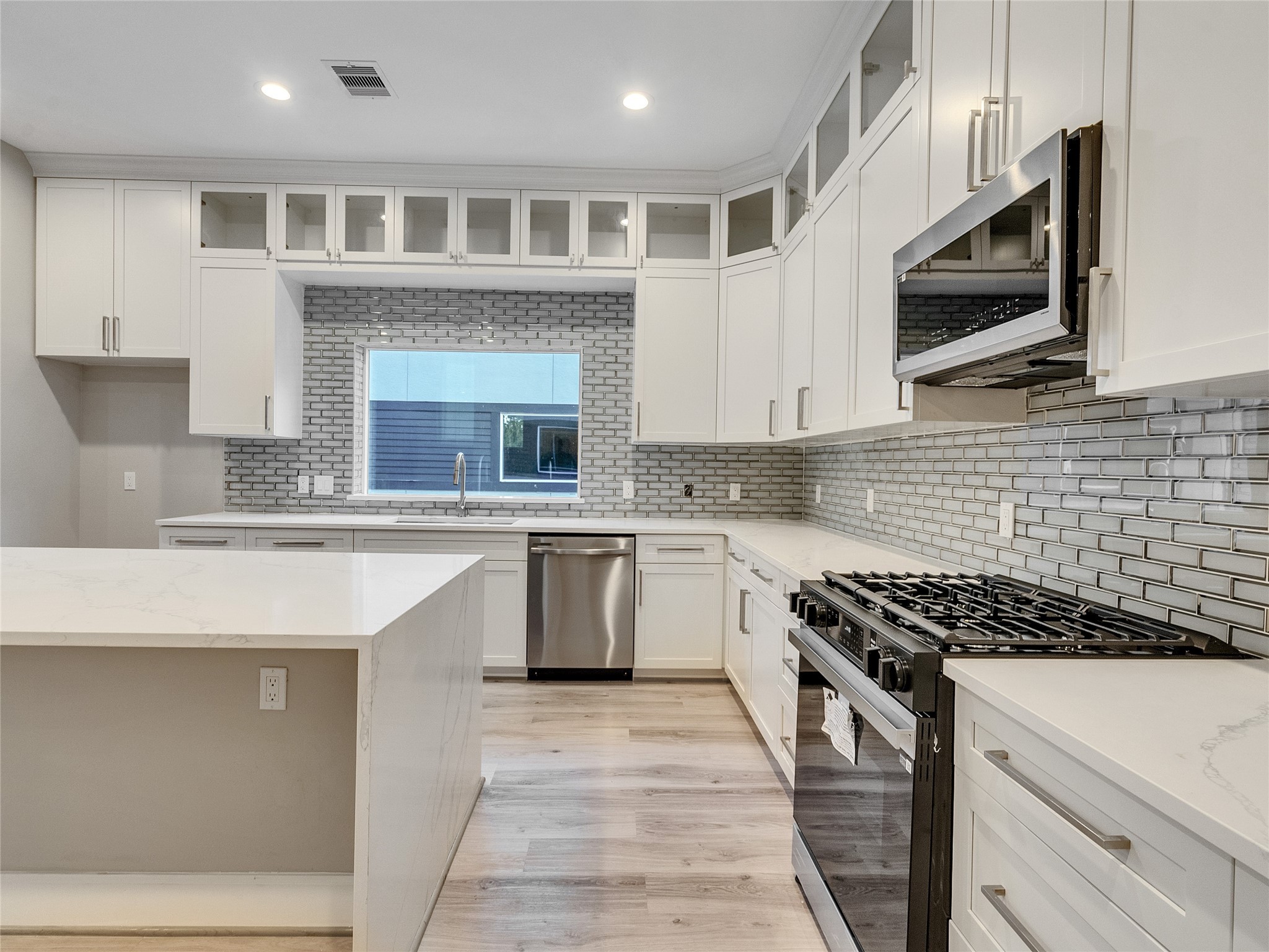1122 West 16th Street, Unit D Houston, TX 77008 - Photo 23 of 40 a kitchen with stainless steel appliances kitchen island granite countertop a stove top oven a sink dishwasher a microwave oven with cabinets and wooden floor
