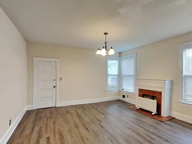 an empty room with wooden floor fireplace and windows