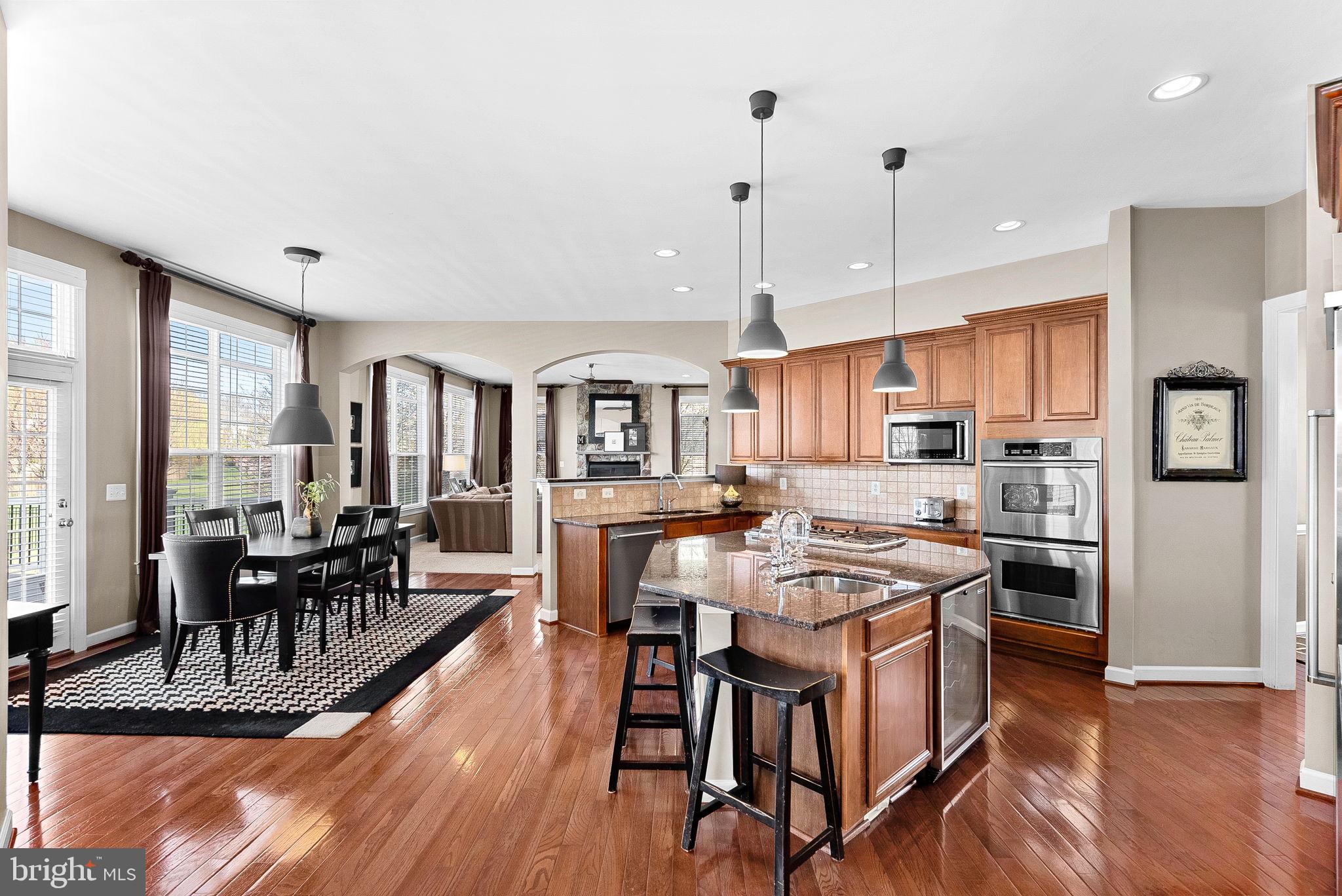 22461 Terra Rosa Place Ashburn, VA 20148 - Photo 12 of 67 a kitchen with stainless steel appliances granite countertop a stove a refrigerator a kitchen island a dining table and chairs with wooden floor