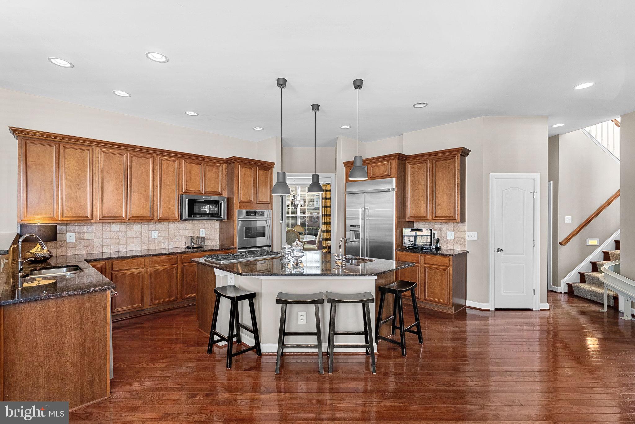 22461 Terra Rosa Place Ashburn, VA 20148 - Photo 15 of 67 a kitchen with stainless steel appliances granite countertop a stove top oven a sink a dining table and chairs with wooden floor