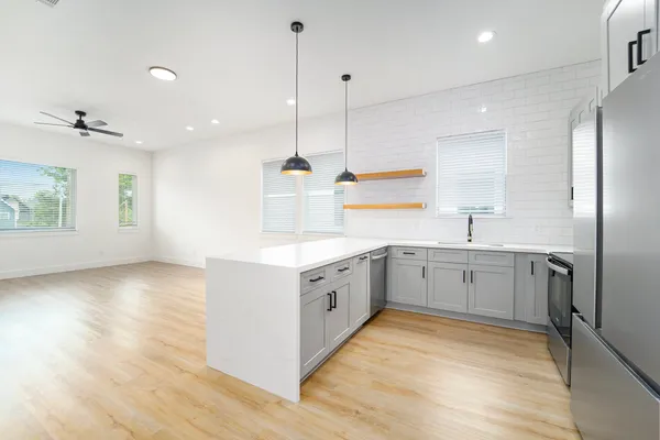 a large white kitchen with a large window a sink stainless steel appliances and cabinets