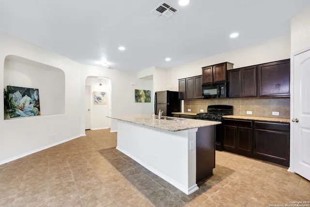 a kitchen with stainless steel appliances granite countertop a stove top oven a sink a refrigerator and white cabinets with wooden floor