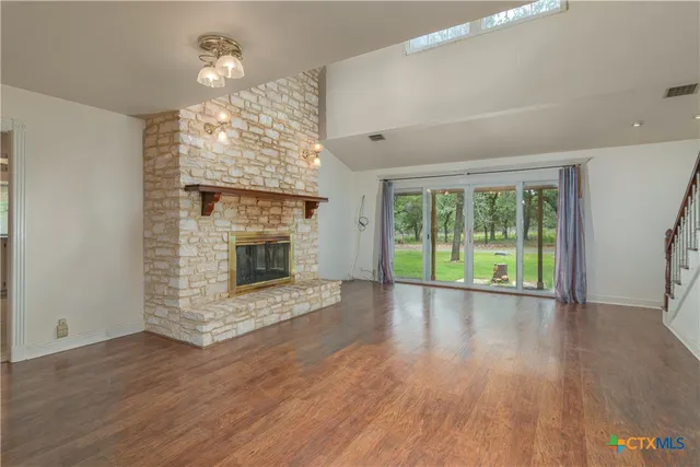 a view of an empty room with wooden floor fireplace and a window