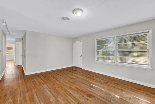a view of an empty room with wooden floor and a window