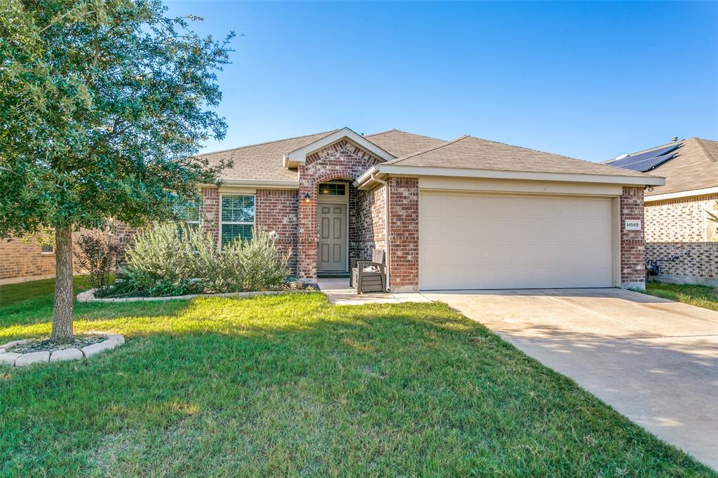 Single story home featuring an attached garage, concrete driveway, a shingled roof, a front yard, and brick siding