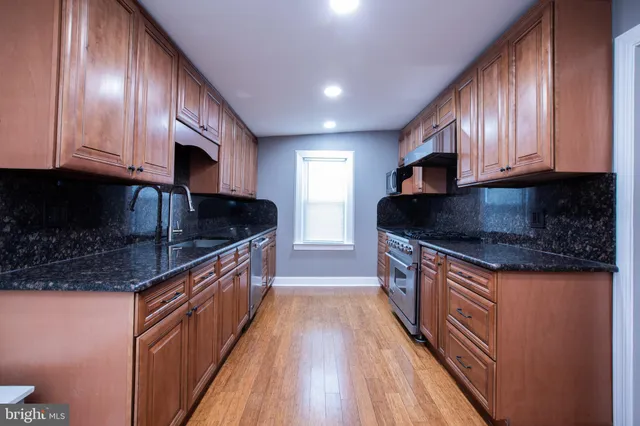 a kitchen with stainless steel appliances granite countertop wooden cabinets a sink and dishwasher a stove top oven with wooden floor