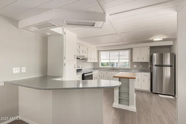 a kitchen with stainless steel appliances granite countertop a refrigerator a sink dishwasher a stove and white cabinets with wooden floor