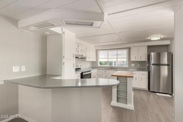 a kitchen with stainless steel appliances granite countertop a refrigerator a sink dishwasher a stove and white cabinets with wooden floor