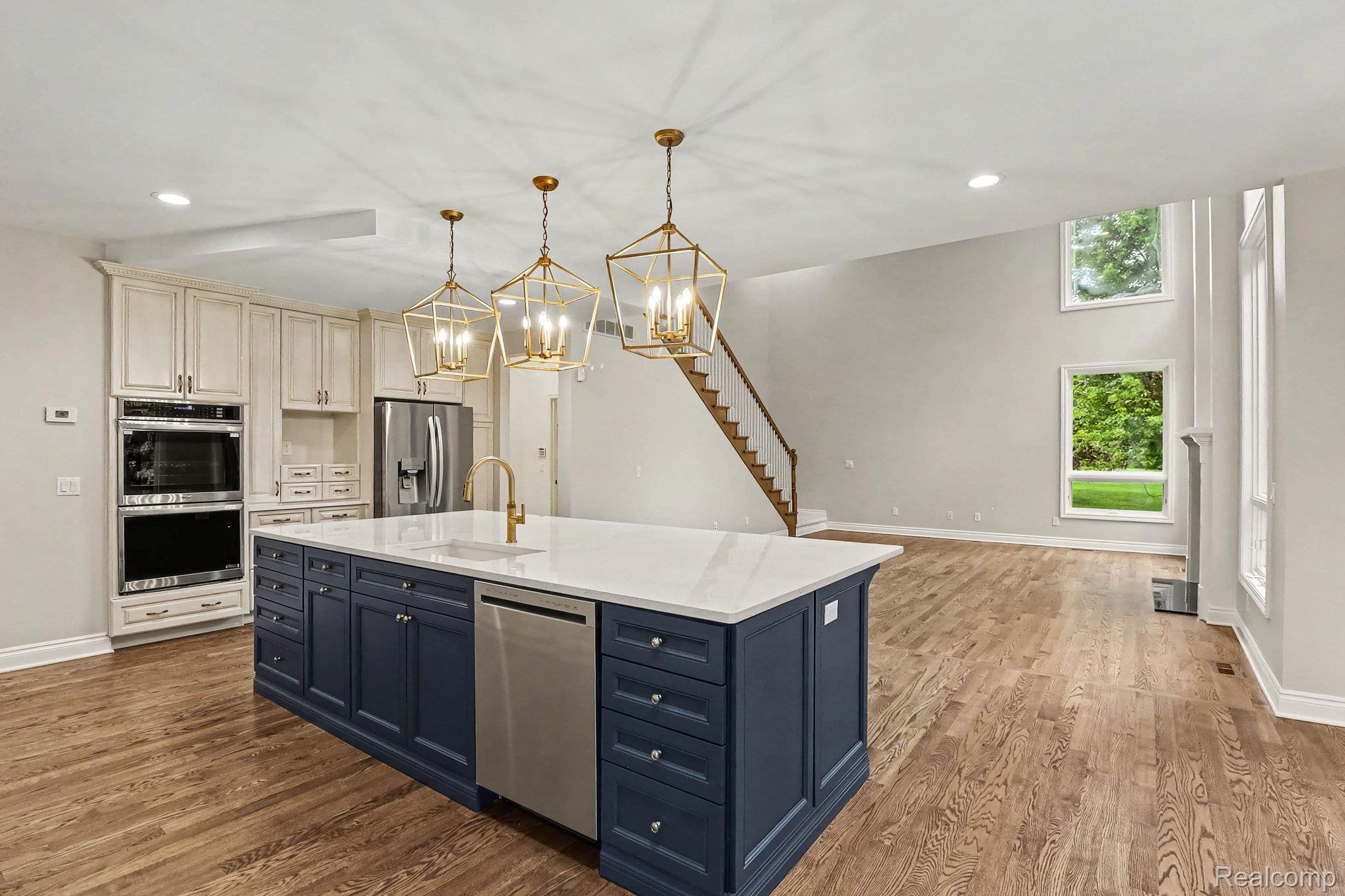 4875 Green Meadow Lane Rochester, MI 48306 - Photo 12 of 60 Spacious kitchen featuring a large central island with a white countertop and blue cabinetry, double wall ovens, and wood-finish flooring
