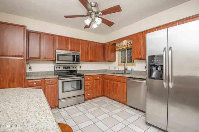 a kitchen with stainless steel appliances granite countertop a stove top oven a refrigerator a sink a dining table and chairs