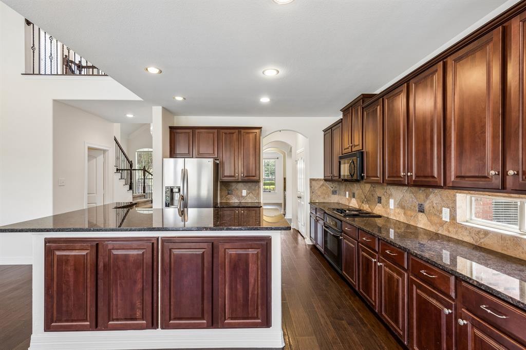 960 Remuda Road Frisco, TX 75033 - Photo 32 of 39 Spacious kitchen featuring rich wood cabinetry, dark stone countertops, stainless steel appliances, a tiled backsplash, and wood-finish flooring