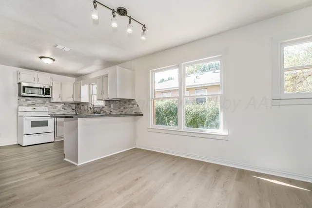 a kitchen with granite countertop a stove a sink dishwasher a refrigerator and white cabinets with wooden floor