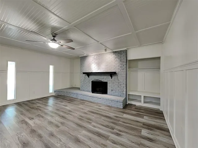 an empty room with wooden floor a ceiling fan a fireplace and windows