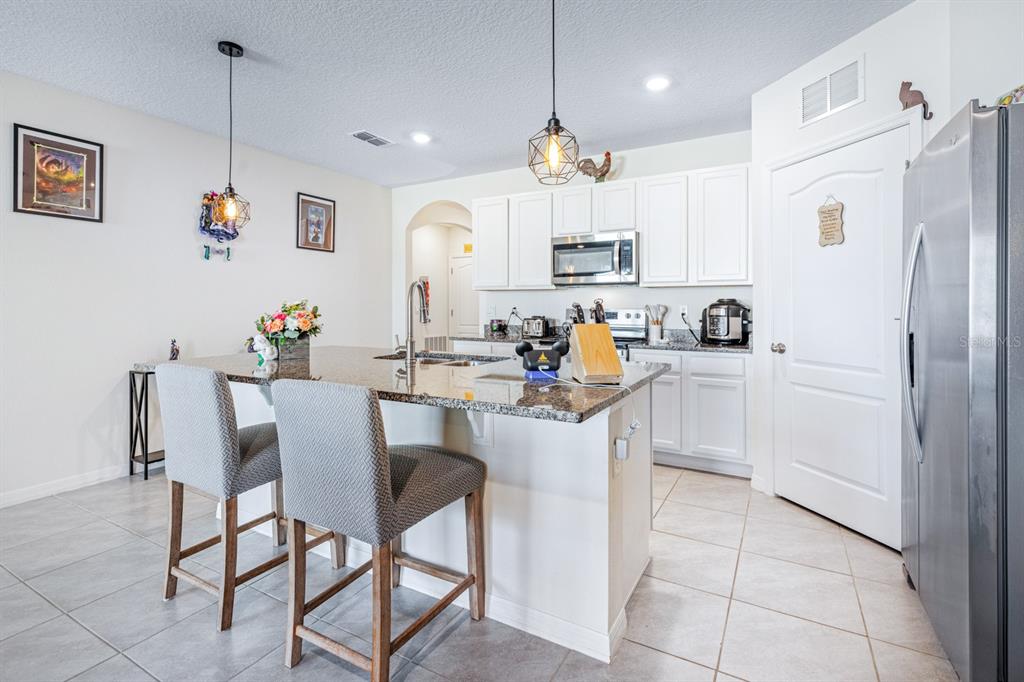 5381 Hickory Downs Way St. Cloud, FL 34771 - Photo 4 of 35 a kitchen with stainless steel appliances kitchen island granite countertop a table chairs and a refrigerator