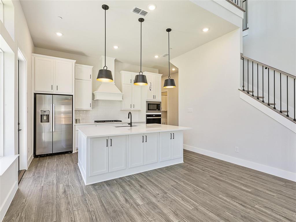 4299 Reeder Rdg Way Frisco, TX 75033 - Photo 11 of 30 a kitchen with stainless steel appliances granite countertop a sink a refrigerator a stove and white cabinets with wooden floor