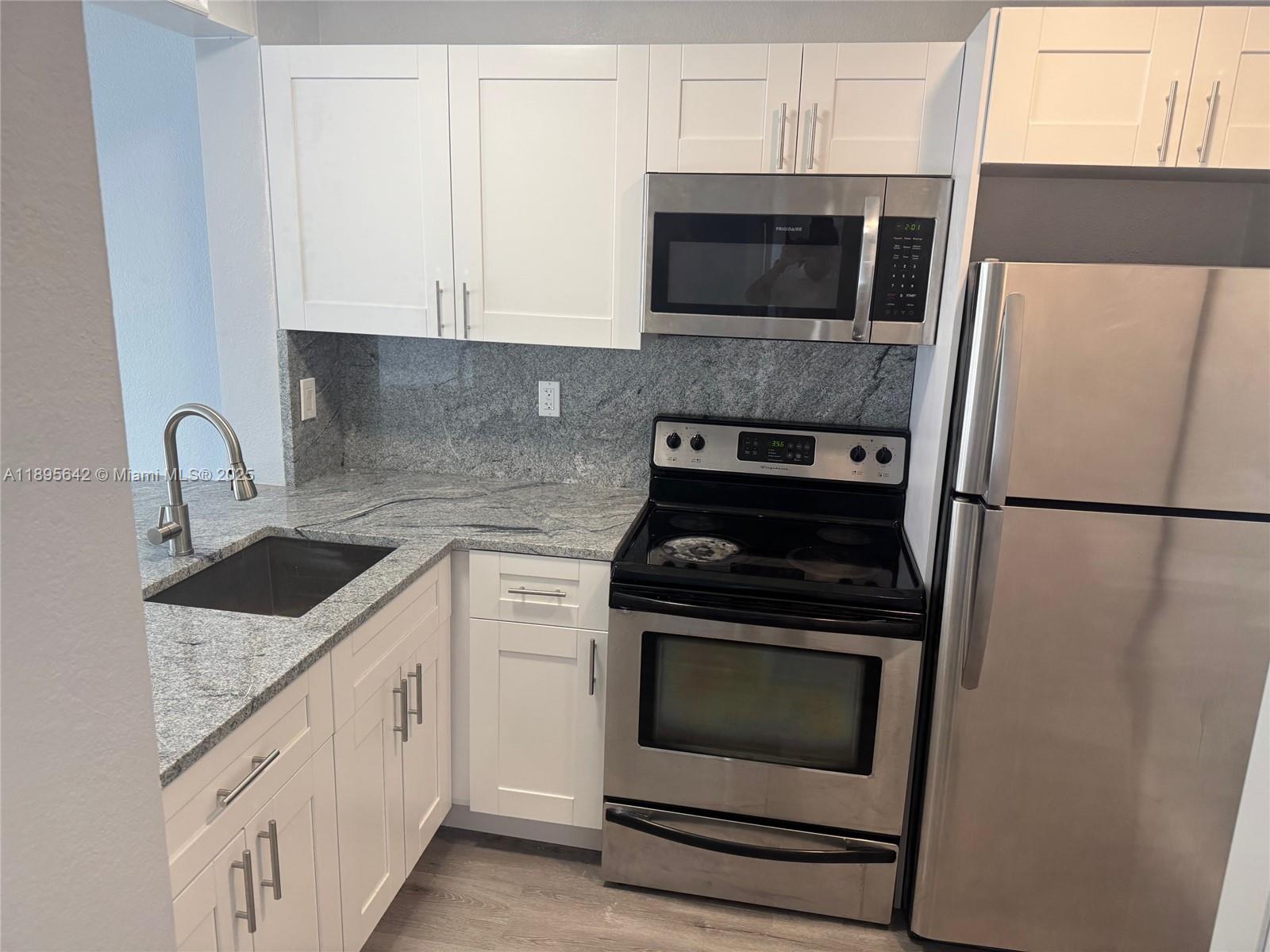 494 Northwest 165th Street, Unit C207 Miami, FL 33169 - Photo 2 of 14 a kitchen with granite countertop white cabinets and stainless steel appliances