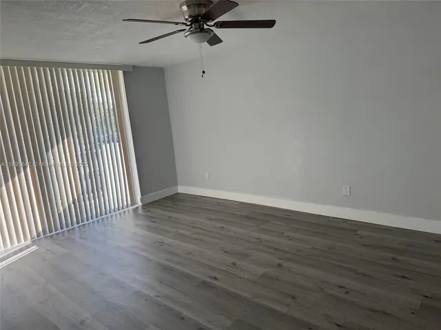 an empty room with wooden floor fan and windows