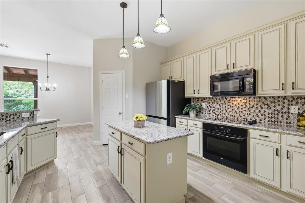 2402 Ravinia Drive Corinth, TX 76208 - Photo 15 of 40 The kitchen features light-colored cabinetry, a central island with a granite countertop, and stainless steel appliances including an oven, microwave, and refrigerator, all convey.