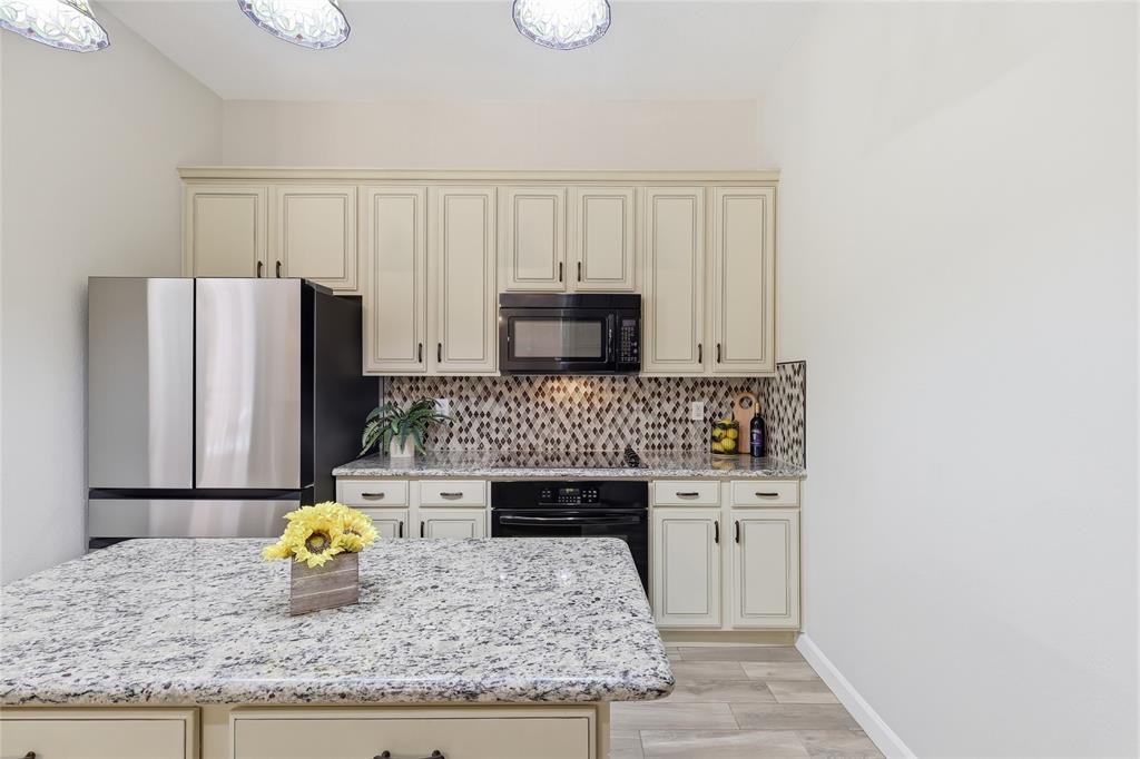2402 Ravinia Drive Corinth, TX 76208 - Photo 16 of 40 The kitchen features a spacious island with a light-colored granite countertop, cream-colored cabinetry, a mosaic tile backsplash, and stainless steel appliances