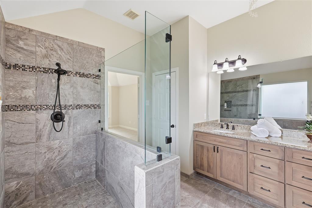 2402 Ravinia Drive Corinth, TX 76208 - Photo 29 of 40 The bathroom features a spacious walk-in shower with tiled walls and a glass partition, complemented by a large vanity with a granite countertop and dual sinks
