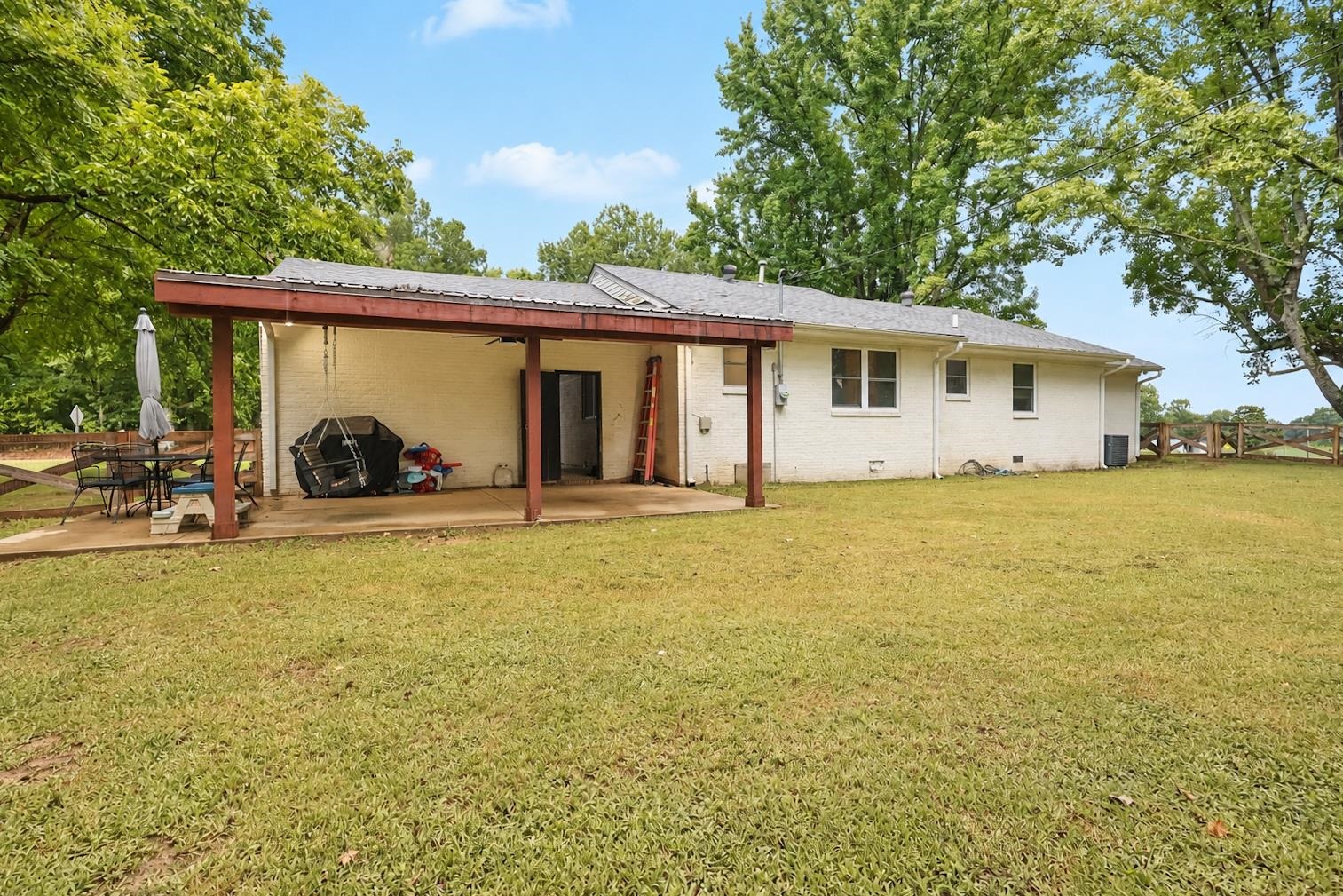 10093 Mt Carmel Road Brighton, TN 38011 - Photo 7 of 36 Expansive backyard featuring a covered patio with a concrete slab, white stucco exterior, multiple windows, and partial perimeter fencing