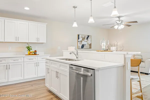 a kitchen with a sink dishwasher and white cabinets with wooden floor