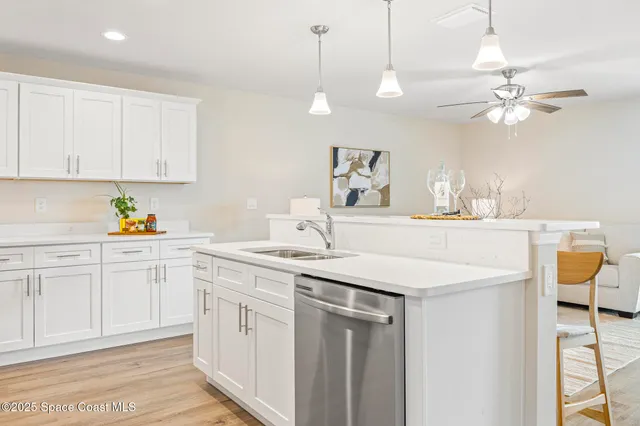 a kitchen with a sink dishwasher and white cabinets with wooden floor