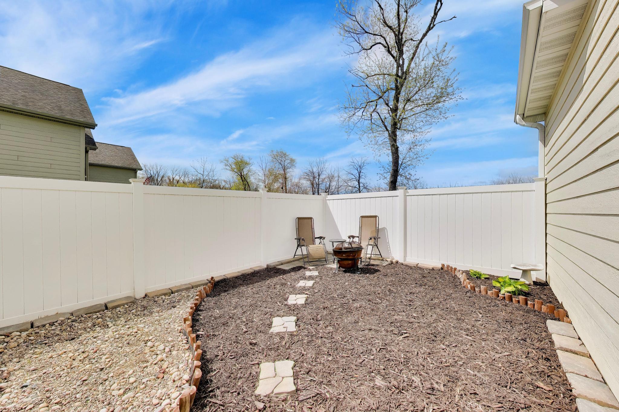 N2392 Mildred Street Delavan, WI 53115 - Photo 29 of 41 Private, white-fenced outdoor nook featuring a stone-lined fire pit area.