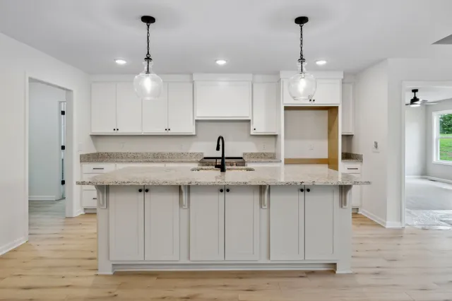 a kitchen with stainless steel appliances granite countertop a sink a stove a refrigerator and white cabinets with wooden floor