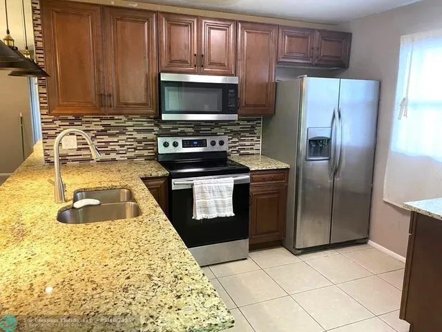 a kitchen with granite countertop a stove a microwave a refrigerator and cabinets