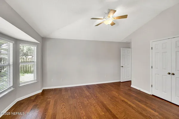 an empty room with wooden floor fan and windows