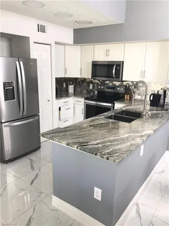 a kitchen with stainless steel appliances granite countertop a refrigerator a stove a sink a microwave a stove and white cabinets