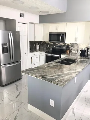 a kitchen with stainless steel appliances granite countertop a refrigerator a stove a sink a microwave a stove and white cabinets