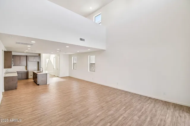 a view of an empty room with wooden floor and a kitchen