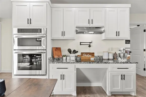 a kitchen with stainless steel appliances granite countertop a stove a sink dishwasher and white cabinets with wooden floor