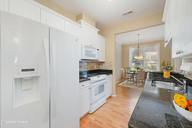 a kitchen with stainless steel appliances granite countertop a stove top oven a sink a dining table and chairs with white cabinets