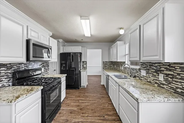 a large kitchen with stainless steel appliances granite countertop a stove top oven a sink dishwasher and a refrigerator with wooden cabinets