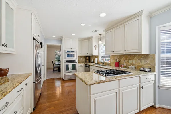 a kitchen with stainless steel appliances granite countertop a stove top oven a sink a refrigerator and white cabinets with wooden floor