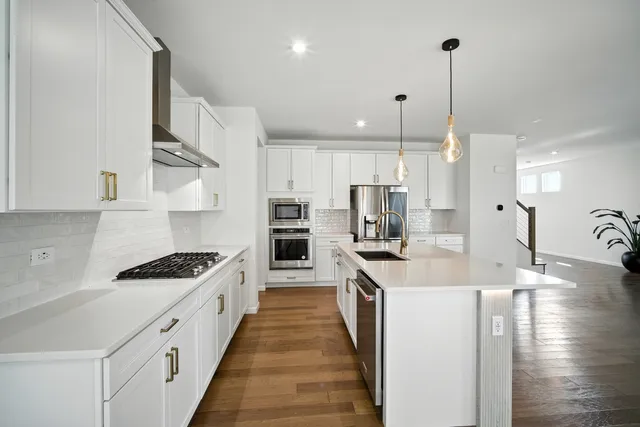 a large kitchen with stainless steel appliances a stove a sink dishwasher and a refrigerator with wooden floor