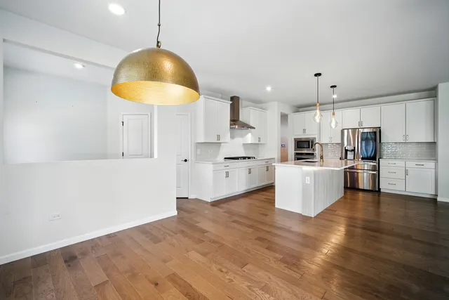 a kitchen with stainless steel appliances kitchen island granite countertop a stove a sink a refrigerator white cabinets and wooden floor